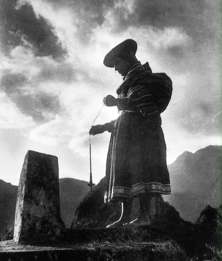 Figura con vestimenta tradicional junto a un monumento de piedra